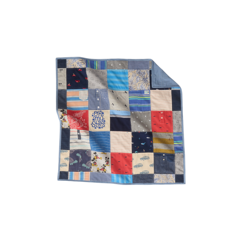 Nice Blanket Little Memories Quilt made from infant and toddler clothes in shades of blue, gray, coral, and cream, featuring stripes, checks, stars, cars, and playful character prints, with a blue backing folded over at the upper right corner.