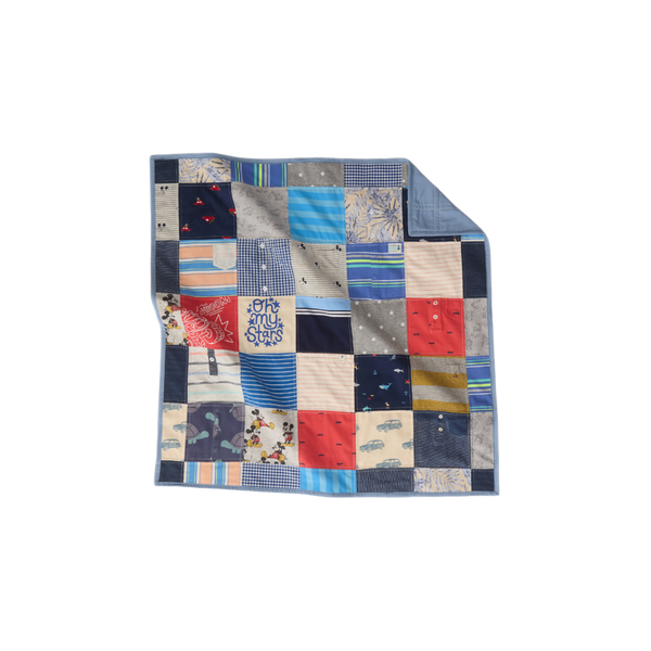 Nice Blanket Little Memories Quilt made from infant and toddler clothes in shades of blue, gray, coral, and cream, featuring stripes, checks, stars, cars, and playful character prints, with a blue backing folded over at the upper right corner.