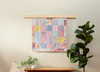 Patchwork memory quilt hanging on a wall with a plant and bench below.