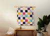 Nice Blanket Little Memories Quilt made from colorful infant and toddler clothes, displayed as wall art above a wooden bench in a warm, neutral room.