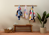Colorful Little Memories memory quilts hanging on a rack against a plain wall with a wooden bench and plant in the foreground.