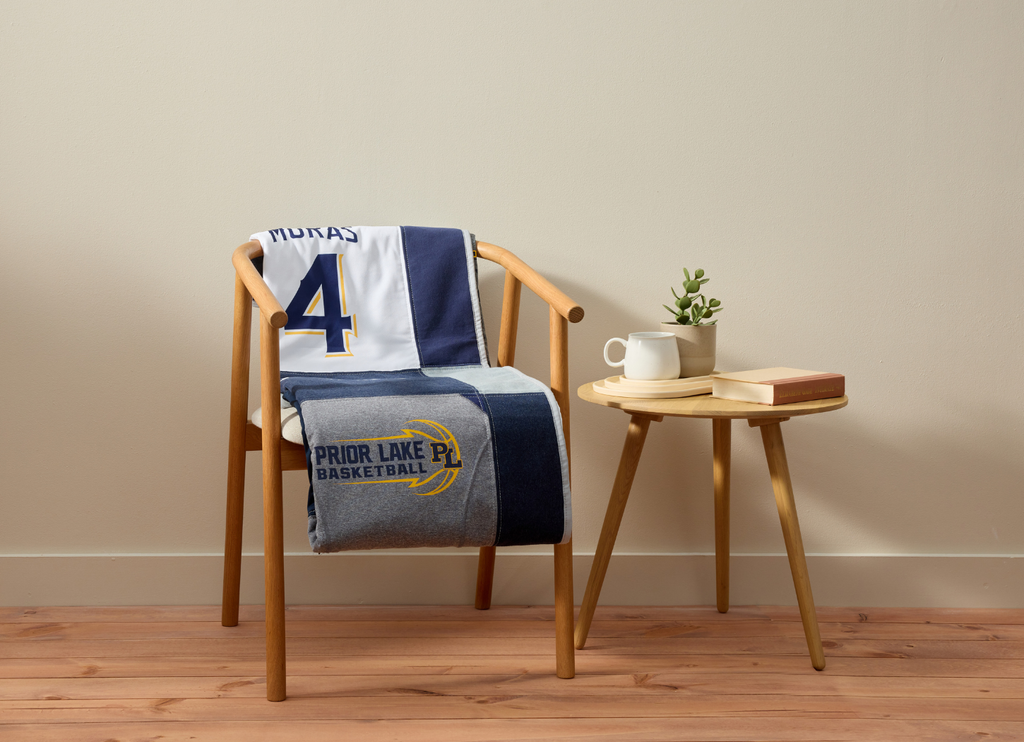 Chair with a sports-themed blanket, a cup, and a book on a small table against a beige wall.