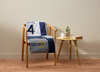 Chair with a sports-themed blanket, a cup, and a book on a small table against a beige wall.