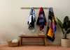 Colorful memory quilts hanging on a rack against a plain wall with a wooden bench and decor items.