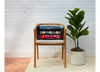 Wooden chair with folded memory quilts on it, next to a potted plant against a white brick wall.